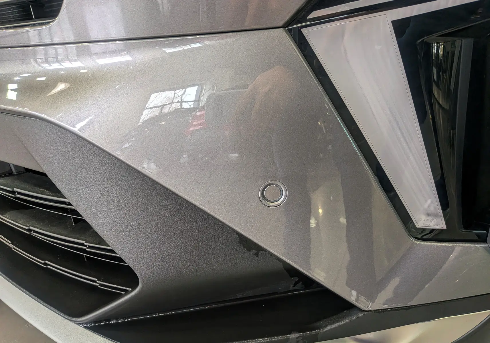 Détail du pare-chocs avant gris Cassiopé du Renault Symbioz E-Tech avec capteur de stationnement circulaire.