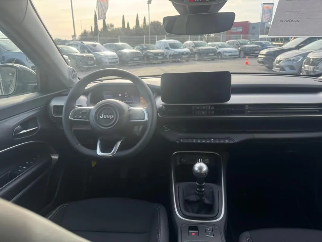 Vue intérieure avant du Jeep Avenger gris 2025, mettant en valeur le volant, la boîte manuelle et l'écran central.