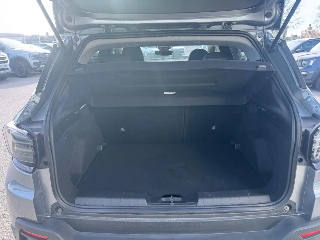 Coffre ouvert d’un Jeep Avenger gris 3/4 arrière, montrant l’espace de chargement vide et la plage arrière relevée.