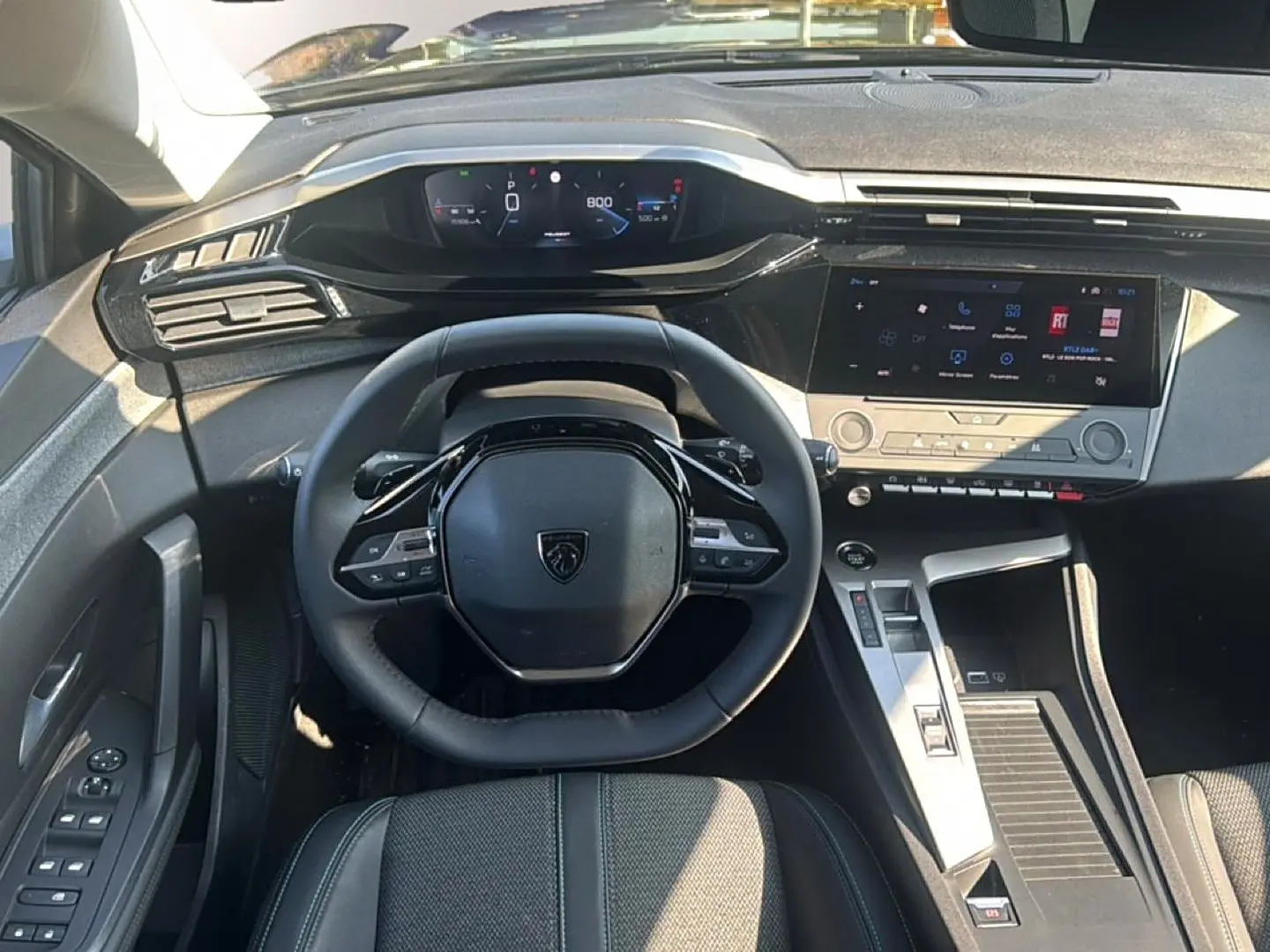 Vue intérieure du poste de conduite de la Peugeot 308 2025, volant multifonction et écran tactile central visibles.