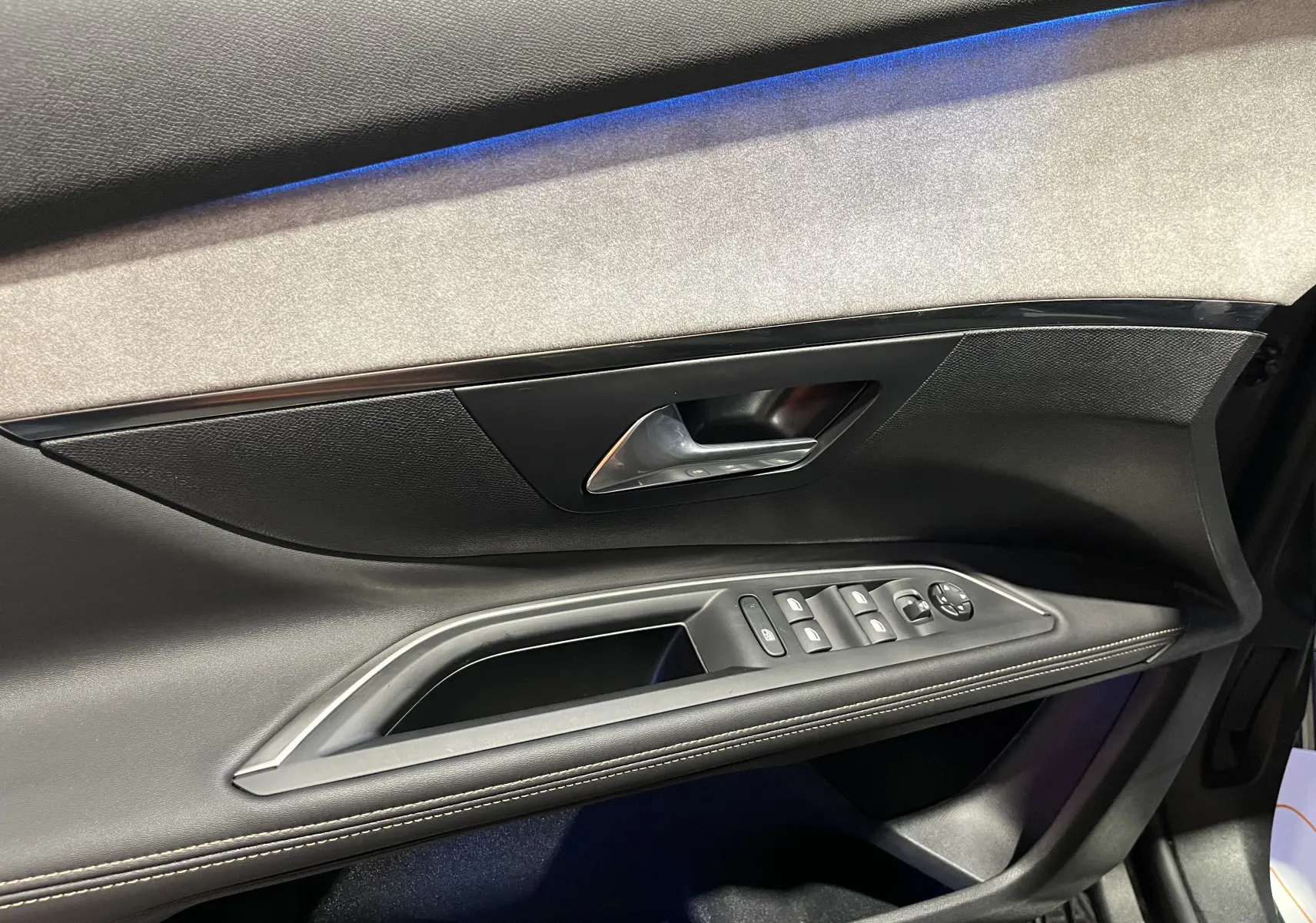 Intérieur côté gauche de la porte avant du Peugeot 5008 GT 2024, avec garniture noire et éclairage d'ambiance bleu.