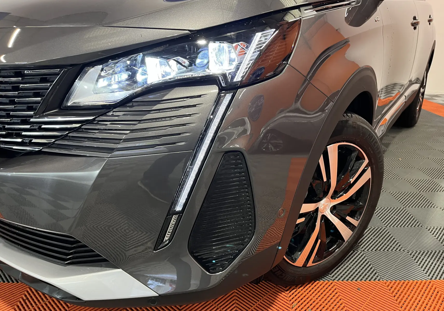 Gros plan sur l'avant droit du Peugeot 5008 gris platinium 2024, mettant en valeur le phare LED et la jante bicolore.