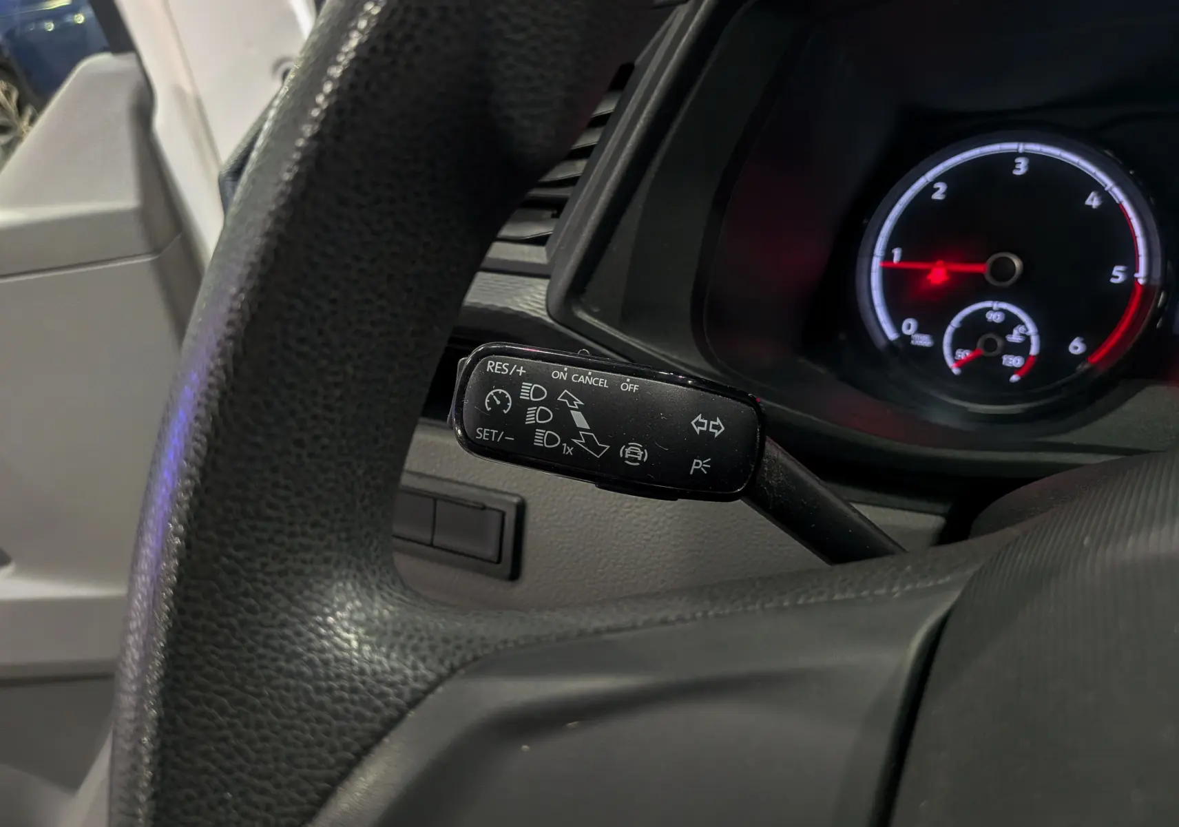 Gros plan sur le commodo de régulateur de vitesse du Volkswagen Transporter 6.1, tableau de bord et volant noirs visibles.