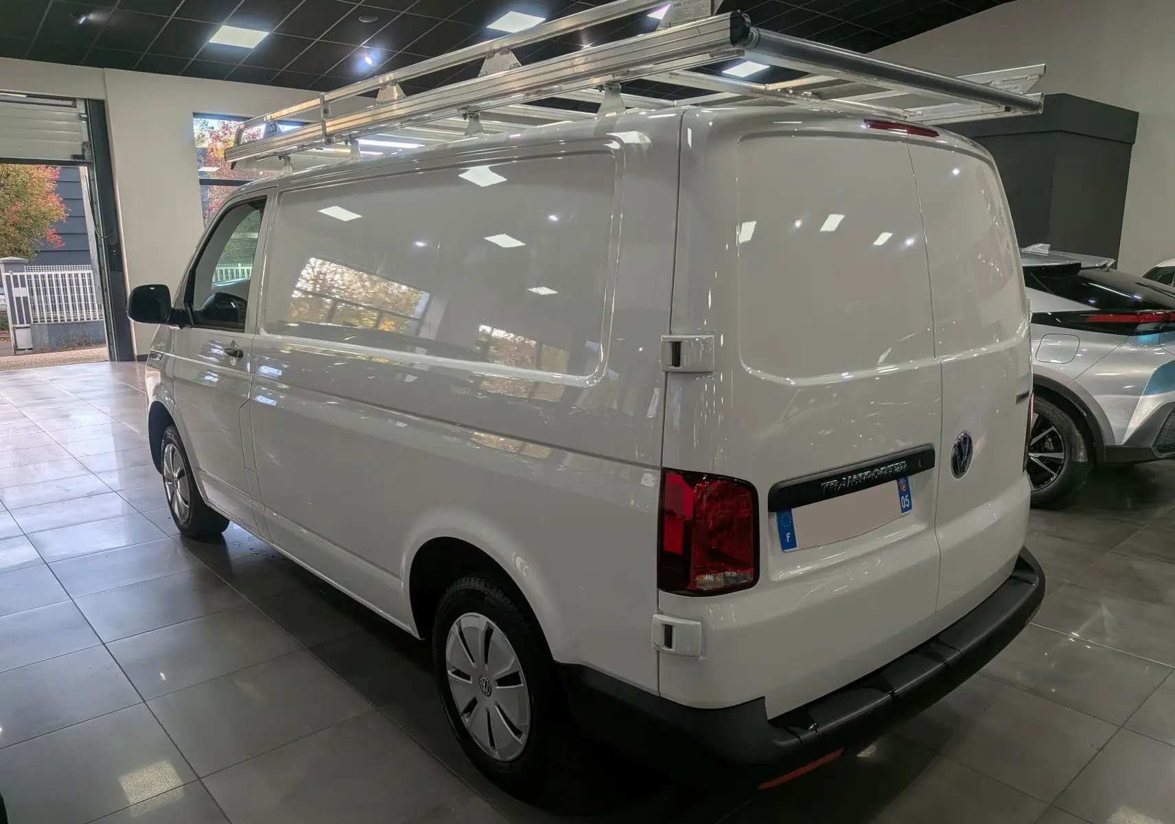 Vue 3/4 arrière droite du Volkswagen Transporter 6.1 Van blanc Candy avec galerie de toit métallique en intérieur showroom.