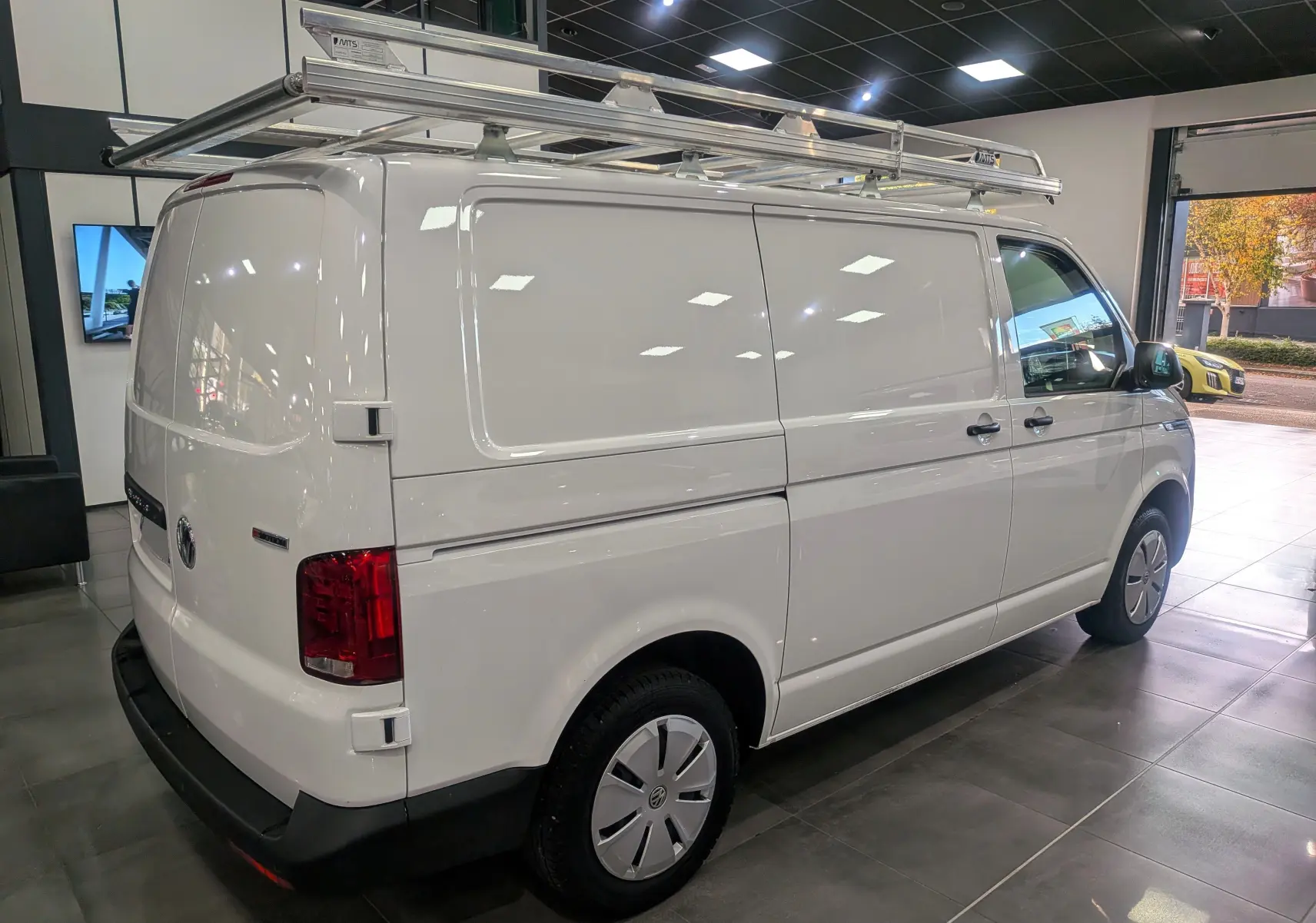 Vue 3/4 arrière droite du Volkswagen Transporter 6.1 Van blanc Candy avec galerie de toit en intérieur showroom.