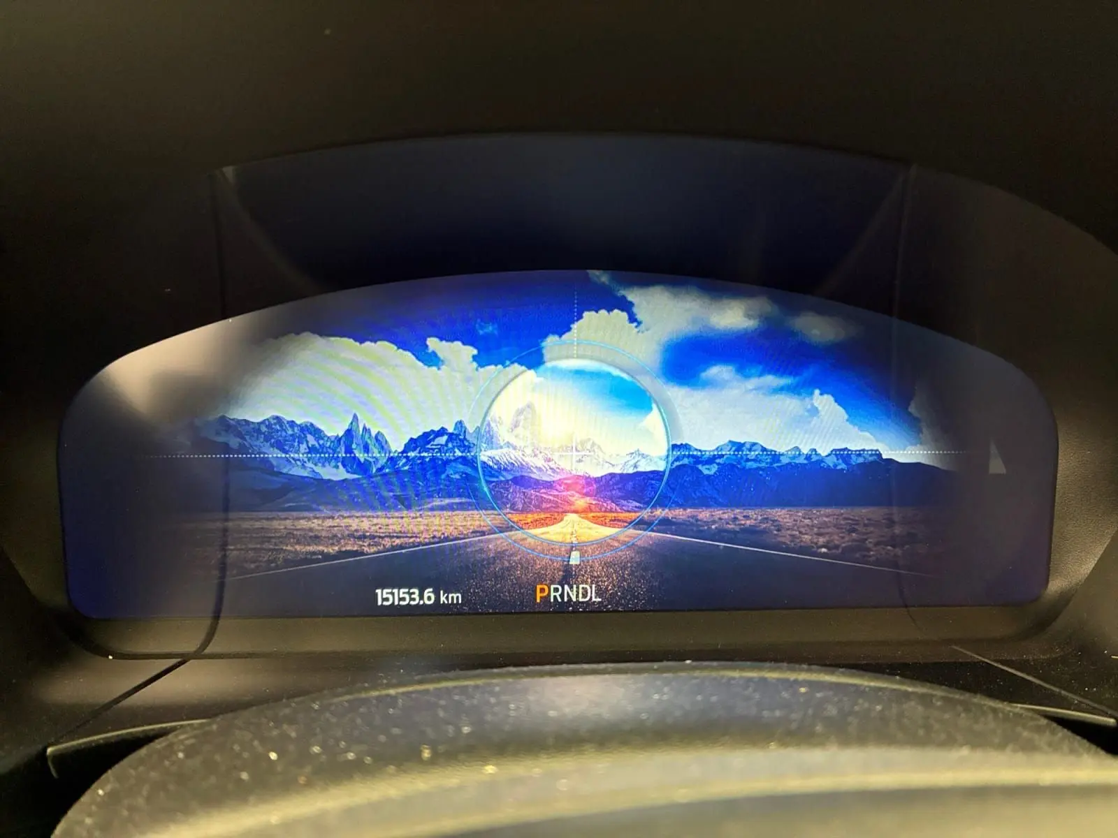 Vue du tableau de bord numérique du Ford Kuga 2024, affichant un paysage montagneux coloré et l'indicateur de boîte automatique.