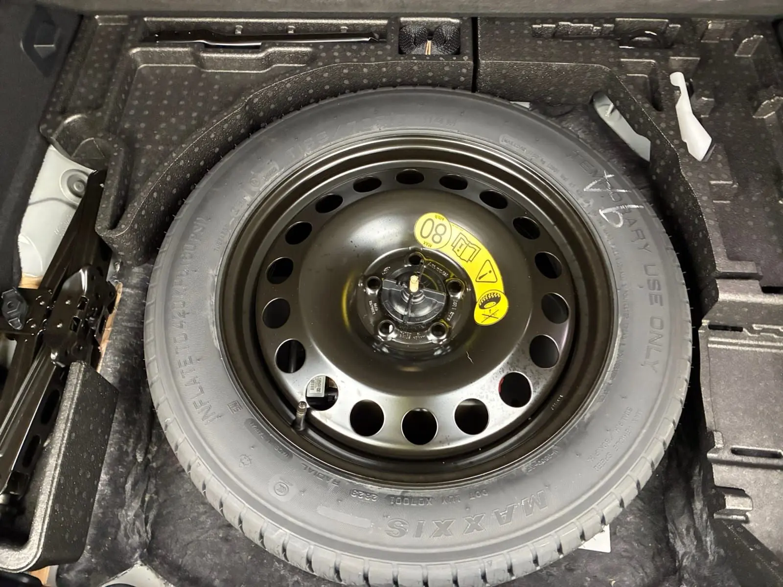 Pneu de secours noir avec jante acier vue de dessus dans le coffre d'un Ford Kuga gris 2024 hybride.