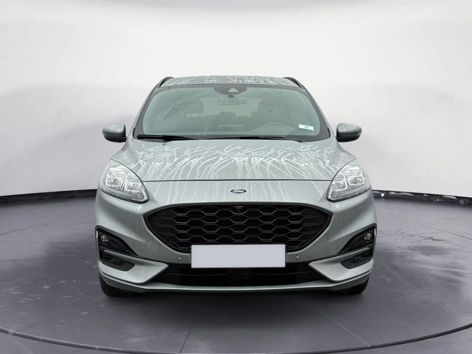 Vue frontale d'un Ford Kuga gris 2024 avec calandre noire et phares LED distinctifs, version hybride essence.