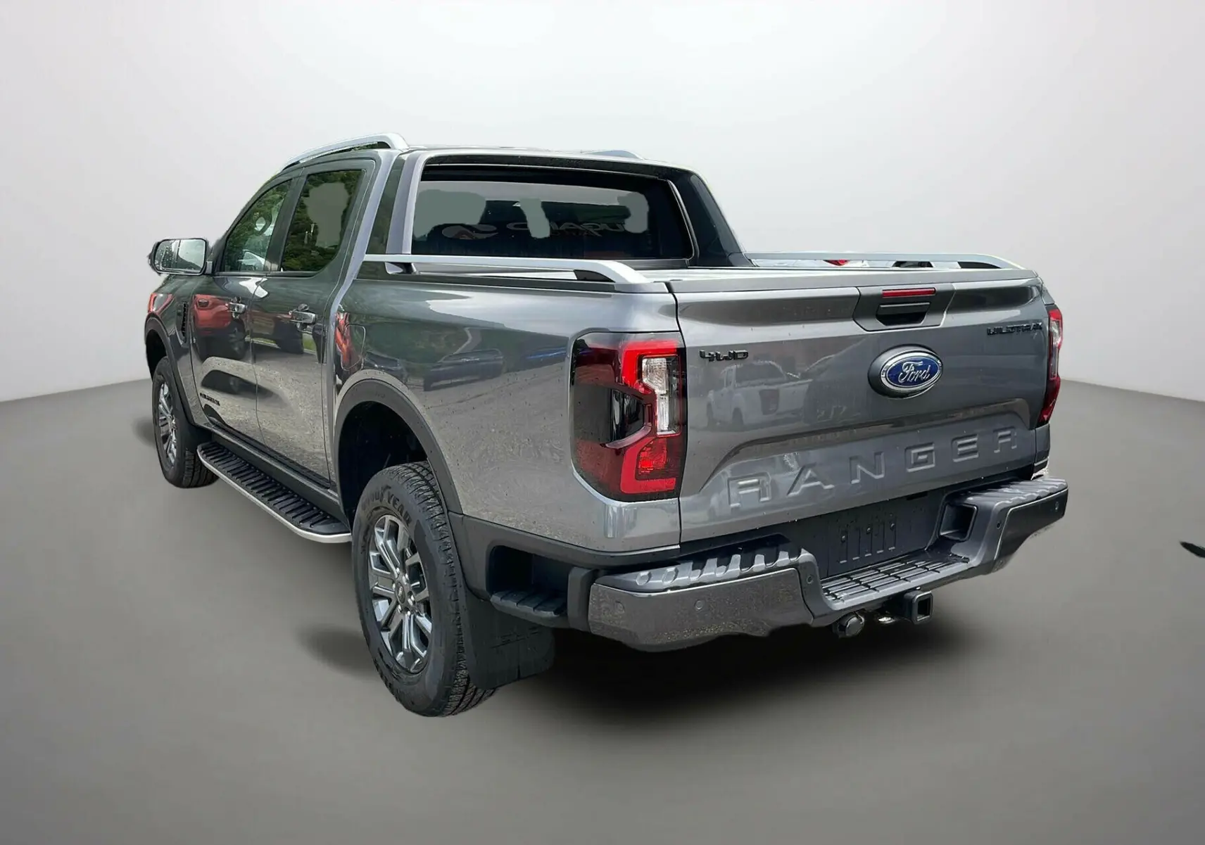 Vue 3/4 arrière droite du Ford Ranger gris carbone avec benne et barres de toit visibles sur fond neutre.