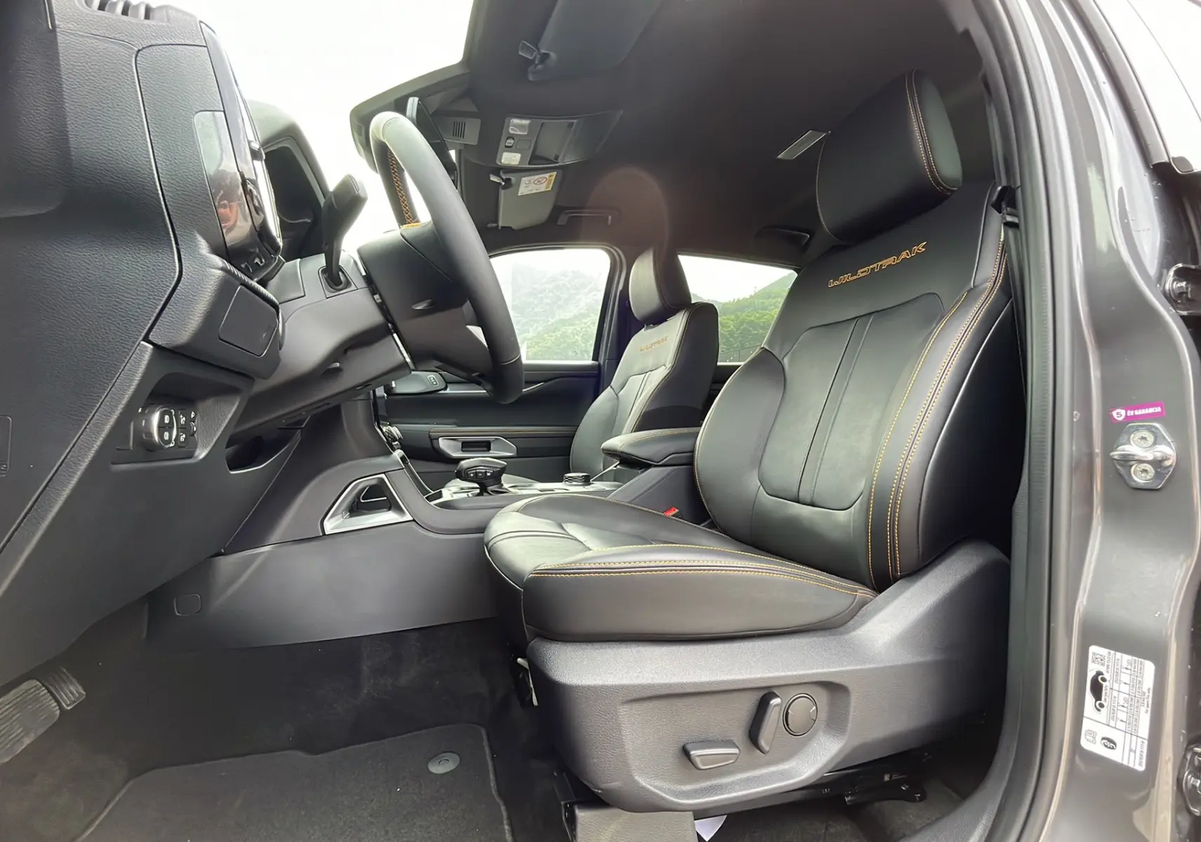 Vue intérieure côté conducteur du Ford Ranger Wildtrak gris carbone, sièges cuir noirs avec surpiqûres orange et logo Wildtrak.