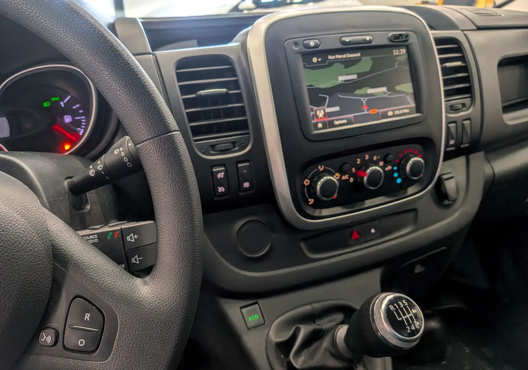 Vue intérieure côté conducteur du tableau de bord du Renault Trafic Fourgon blanc, avec écran GPS et levier de vitesses manuel.
