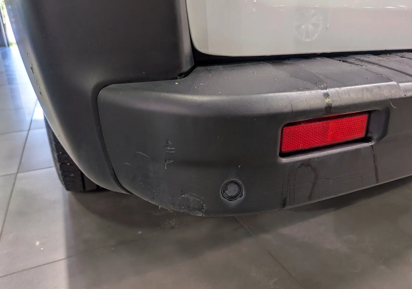 Gros plan sur le pare-chocs arrière droit noir avec un réflecteur rouge du Renault Trafic Fourgon blanc Glacier.