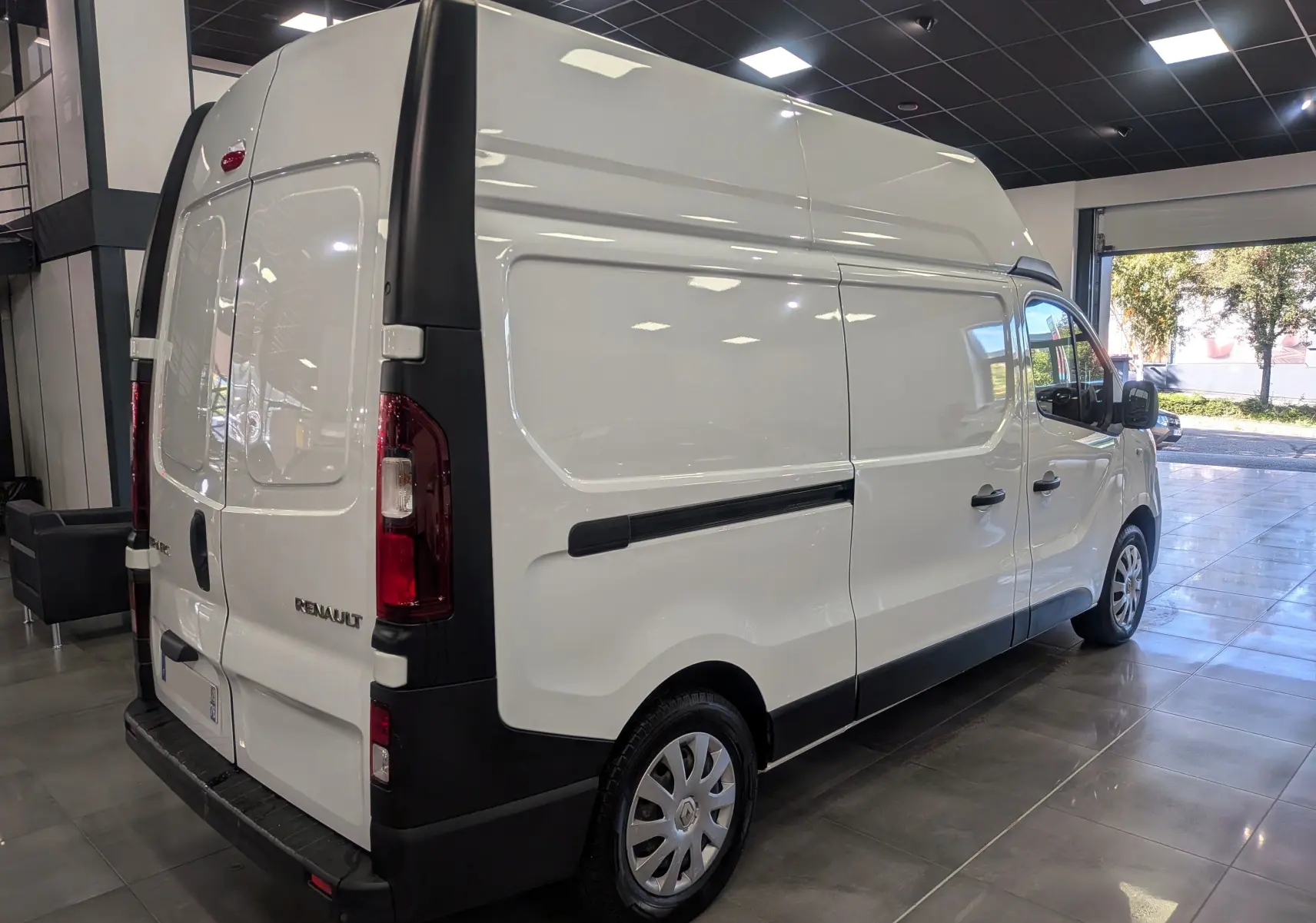 Renault Trafic Fourgon blanc glacier vu en 3/4 arrière droit dans un showroom lumineux avec toit haut L2H2.