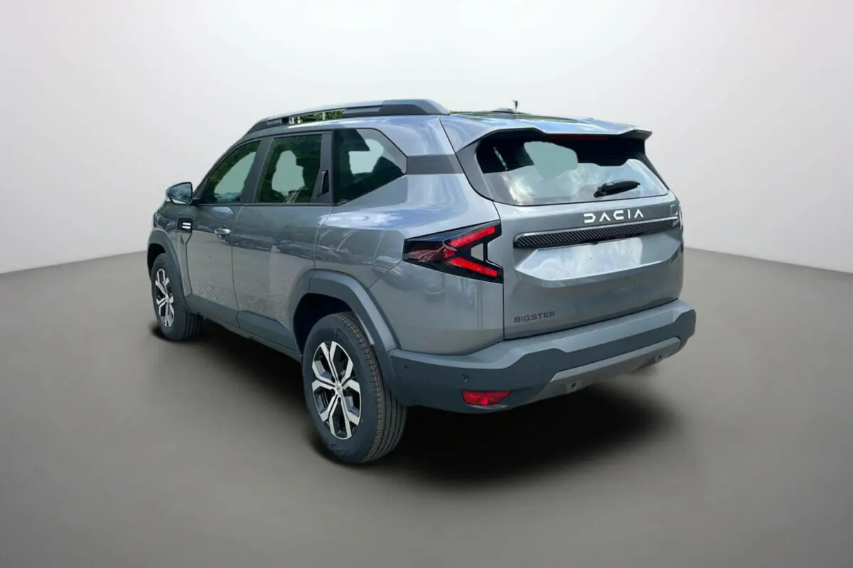 Vue 3/4 arrière droite du Dacia Bigster gris schiste avec barres de toit et jantes alu 17 pouces visibles.