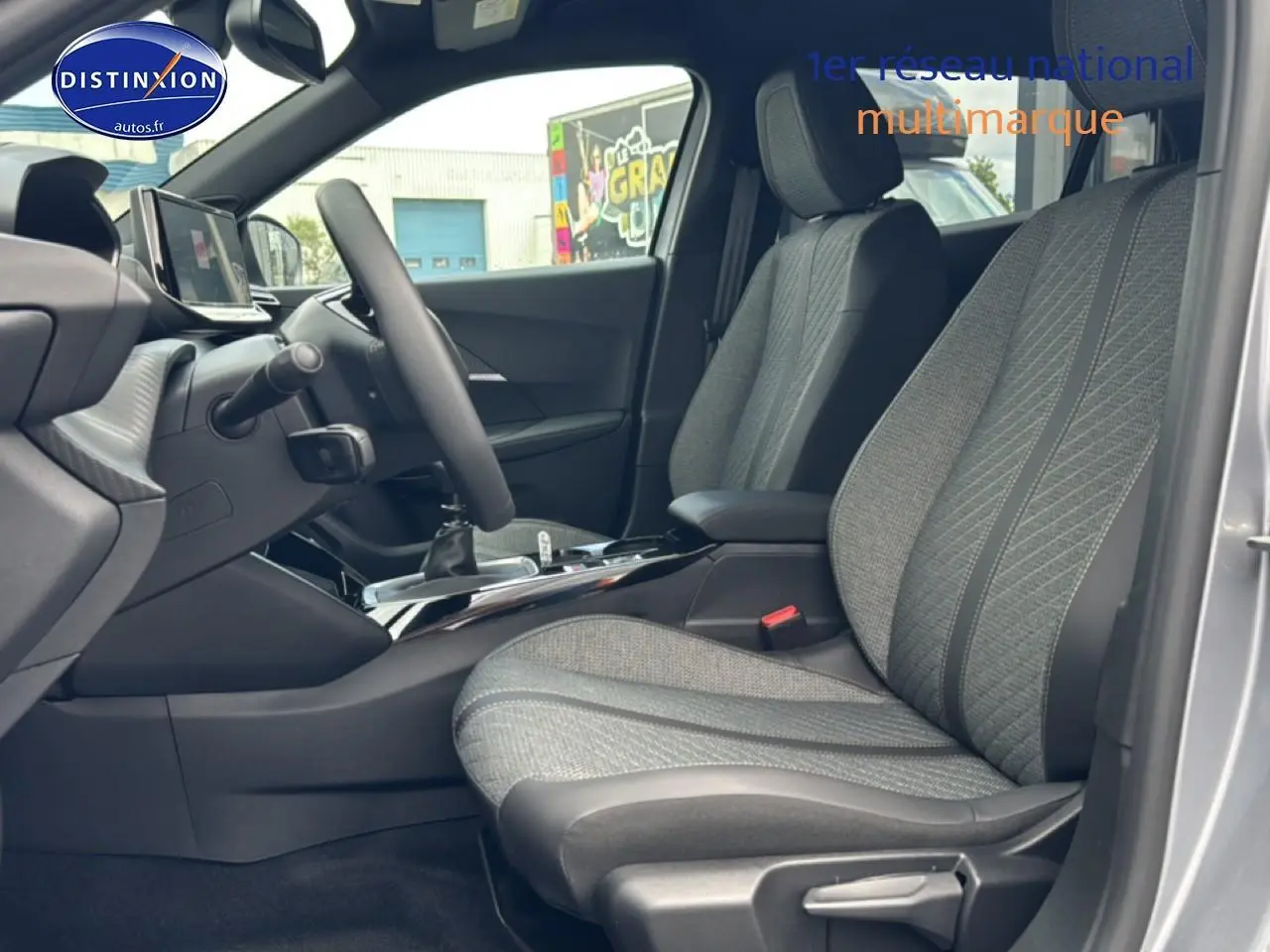 Vue intérieure côté conducteur du Peugeot 2008 gris artense, mettant en valeur les sièges en tissu et la console centrale.