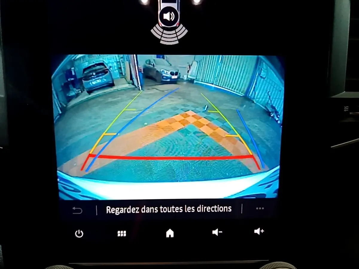 Vue caméra de recul de la Renault Mégane blanche, avec lignes de guidage colorées et vue sur un parking intérieur.