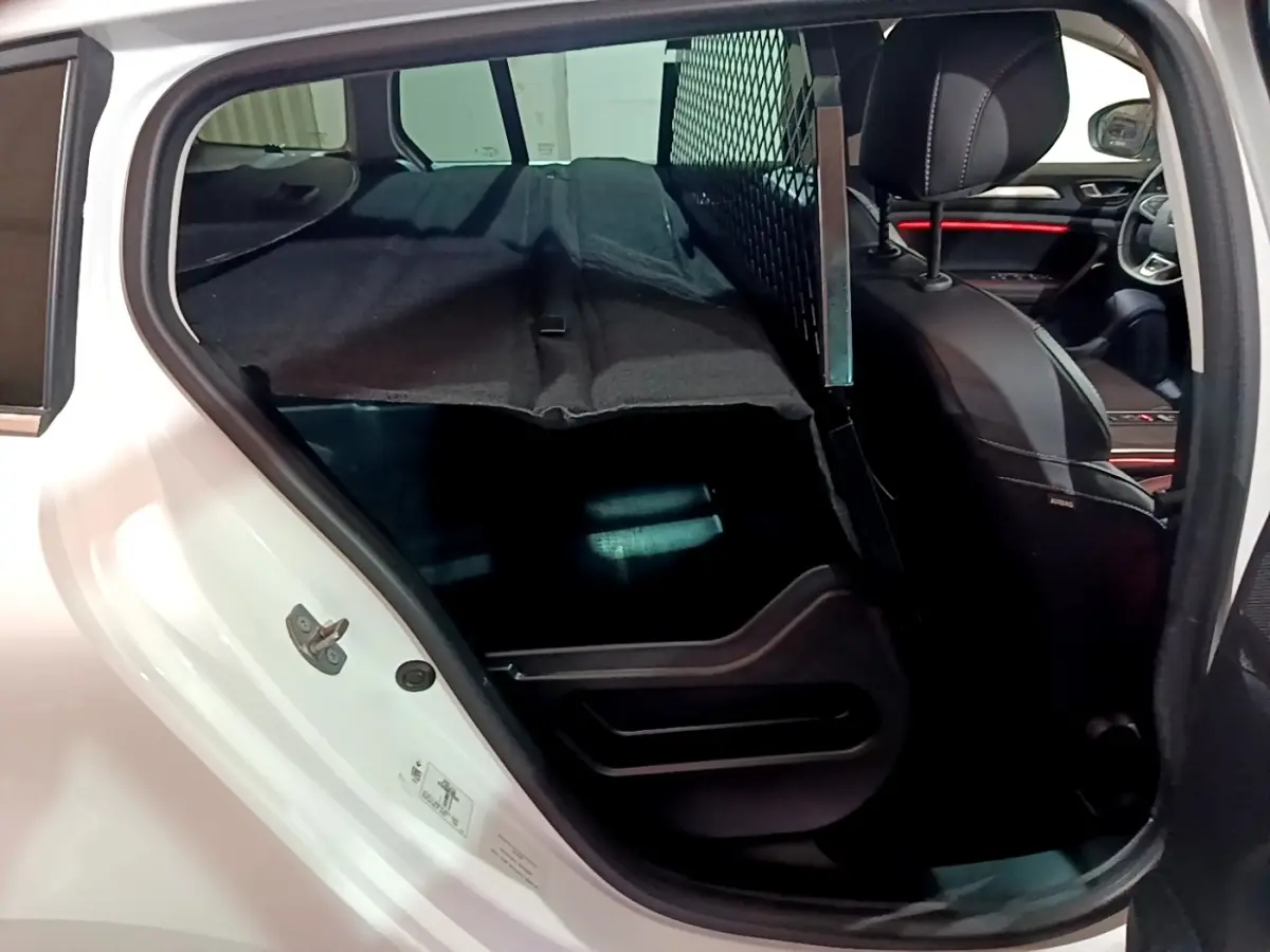 Vue intérieure côté arrière gauche de la Renault Mégane Techno TCe 140 blanche, avec séparation grillagée et banquette rabattue.