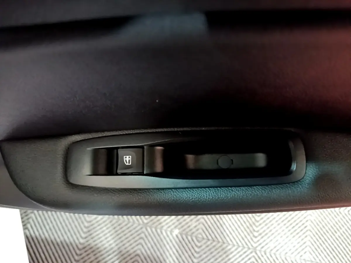 Gros plan sur la commande de lève-vitre électrique noire côté porte intérieure d’une Renault Mégane blanche.