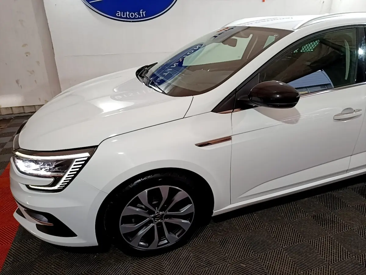 Vue 3/4 avant droit d'une Renault Mégane Techno TCe 140 blanche avec rétroviseur noir et feux LED allumés.
