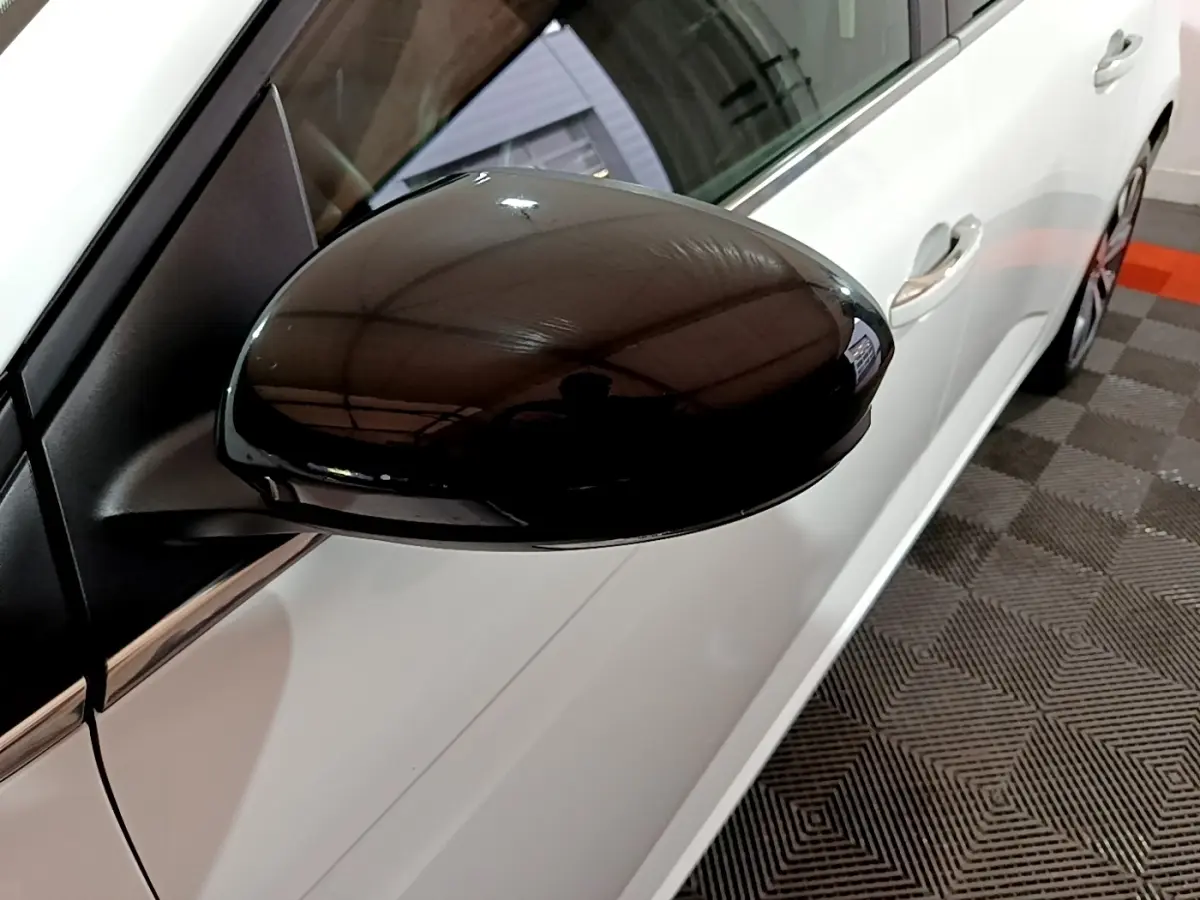 Gros plan sur le rétroviseur noir côté conducteur d’une Renault Mégane blanche vue de profil gauche.