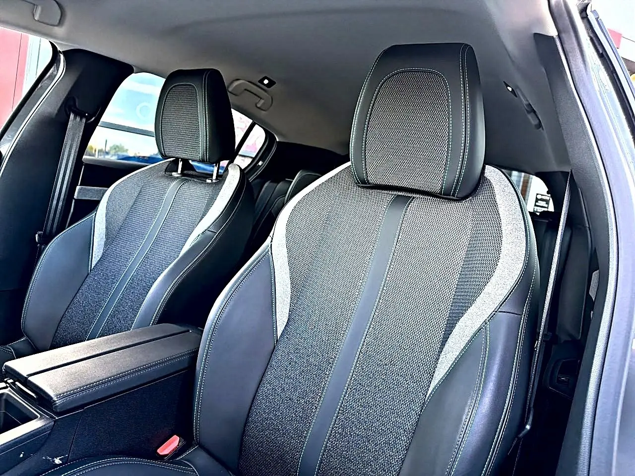 Vue intérieure rapprochée des sièges avant en tissu et cuir noir avec surpiqûres contrastantes dans une Peugeot 308 gris selenium.