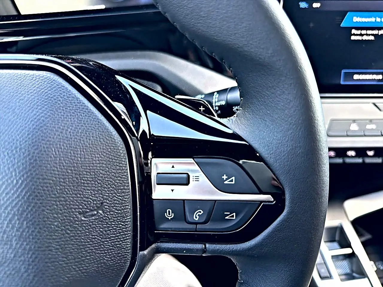 Gros plan sur les commandes du volant multifonction noir de la Peugeot 308 gris selenium, avec écran tactile en arrière-plan.