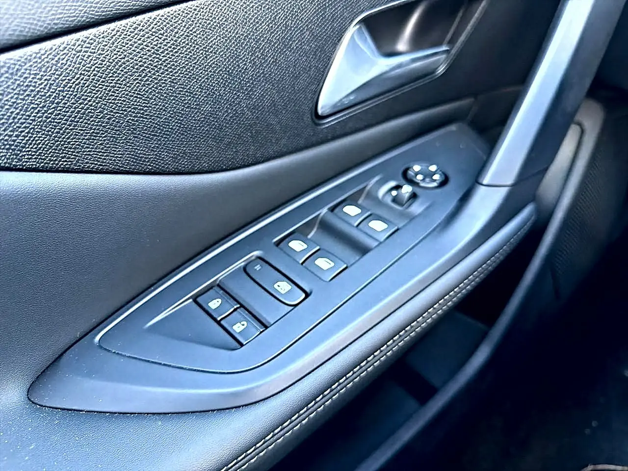Gros plan sur la commande des vitres et rétroviseurs côté conducteur de la Peugeot 308 gris selenium, intérieur noir.
