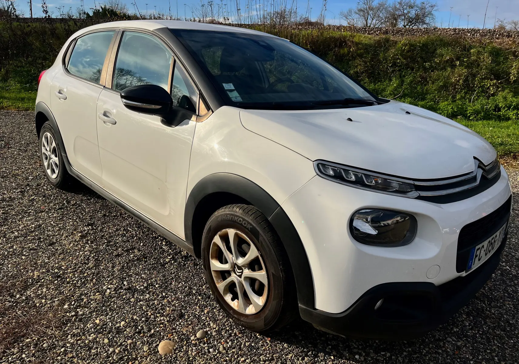 Citroën C3 blanche vue 3/4 avant droit, avec protections noires sur les passages de roues et jantes alliage.