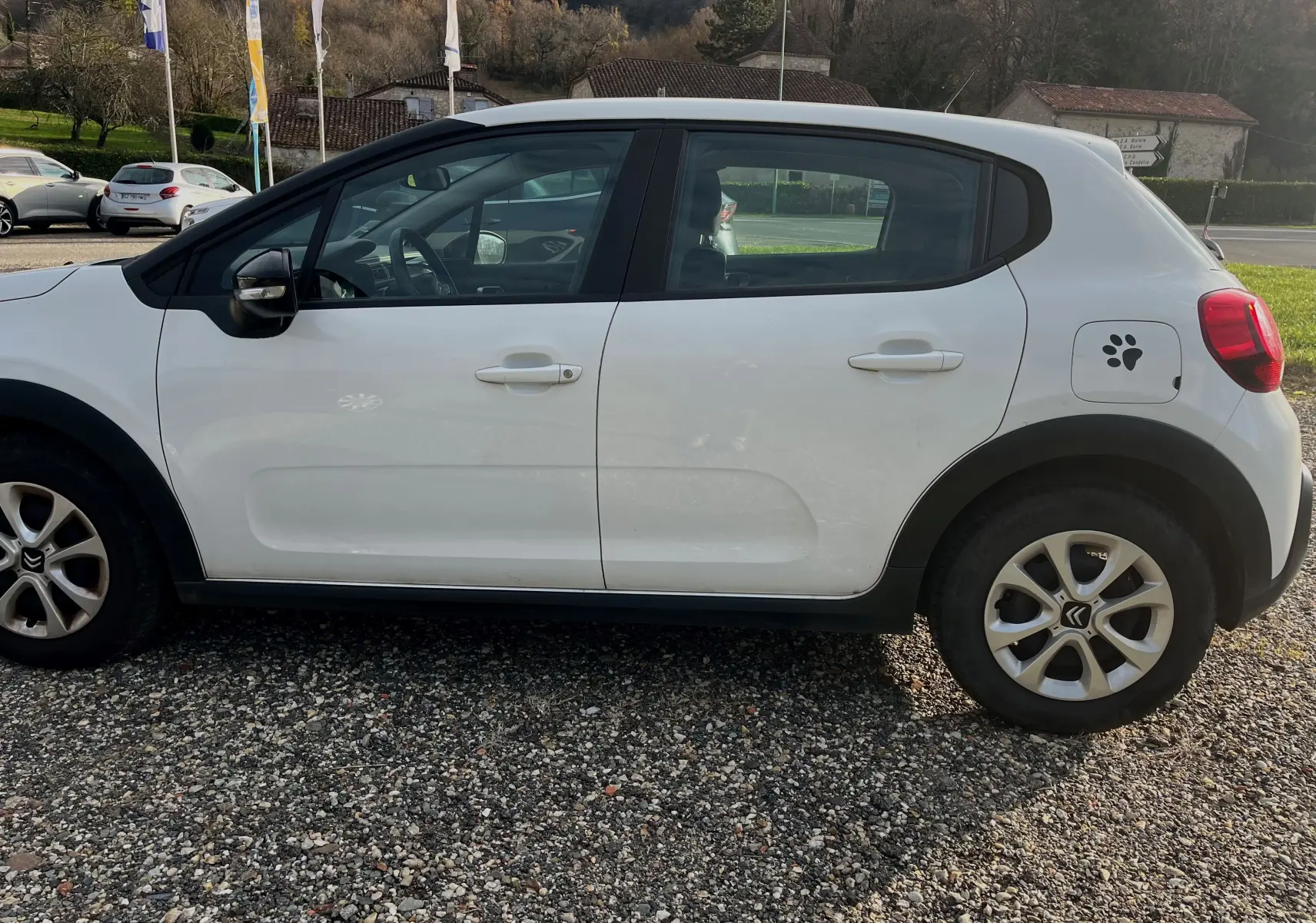 Vue de profil côté gauche d'une Citroën C3 blanche de 2019 avec autocollant patte de chien sur la trappe à carburant.