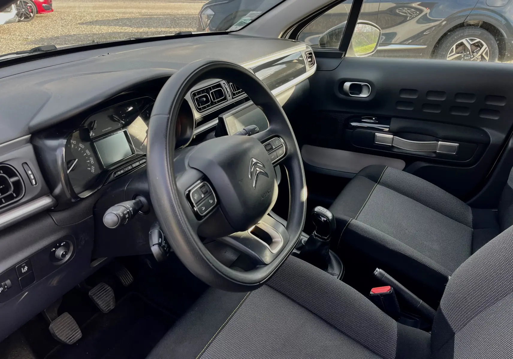 Intérieur de la Citroën C3 blanche 2019, vue côté conducteur montrant volant, tableau de bord et siège avant noir.