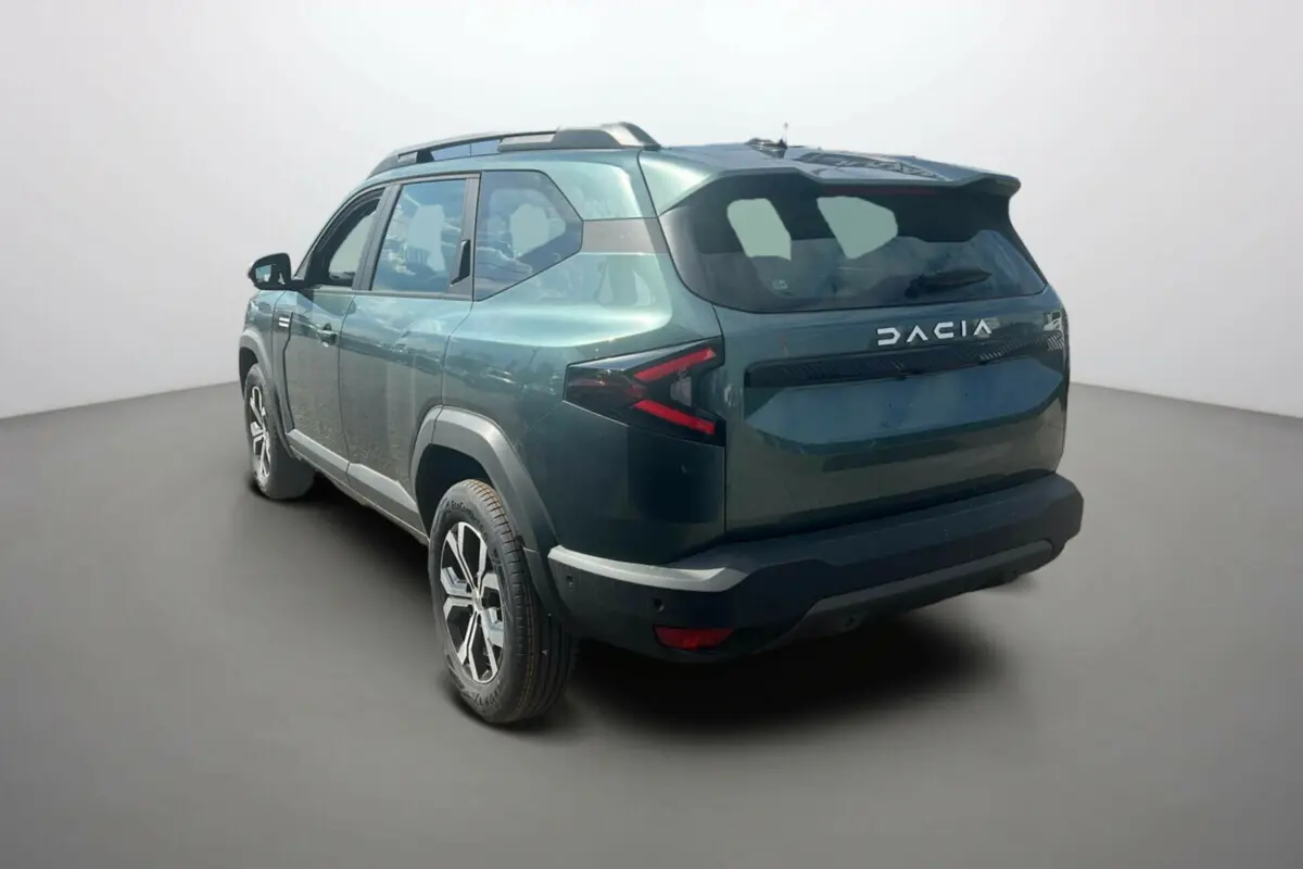 Vue 3/4 arrière droite du SUV Dacia Bigster vert cèdre avec jantes alu 17 pouces et barres de toit visibles.