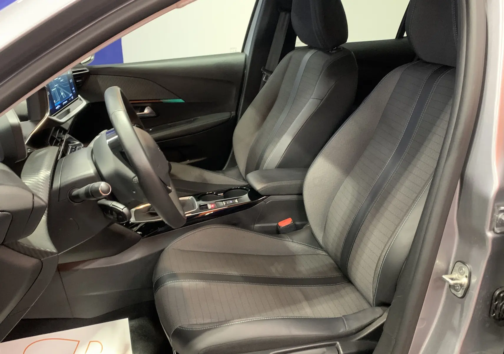 Intérieur de la Peugeot 208 PureTech 100 Allure Business 2021, vue côté conducteur, sièges gris et tableau de bord moderne avec écran GPS.