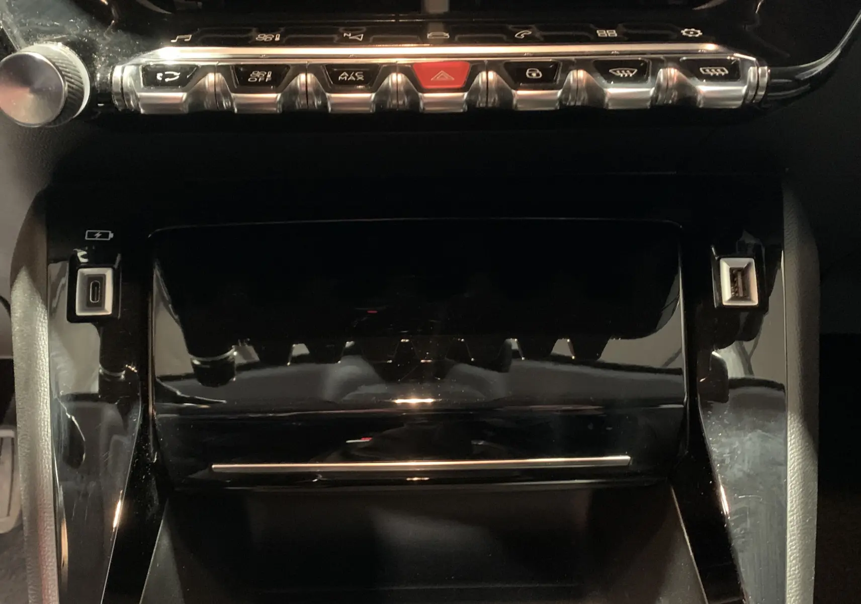 Vue rapprochée de la console centrale noire brillante de la Peugeot 208 PureTech 100 Allure Business avec boutons chromés et ports USB.