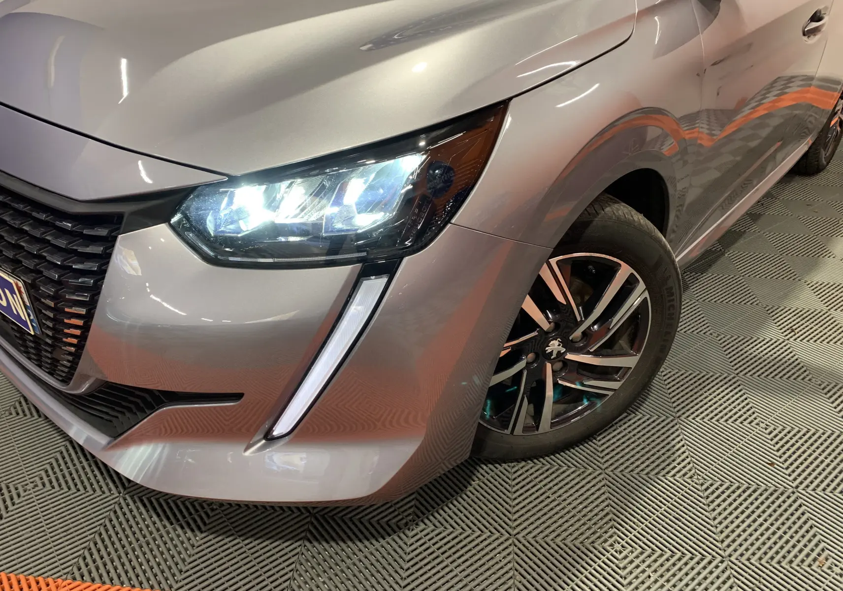 Vue 3/4 avant droit d'une Peugeot 208 gris métallisé avec phares LED allumés et jante alliage noire et argent.