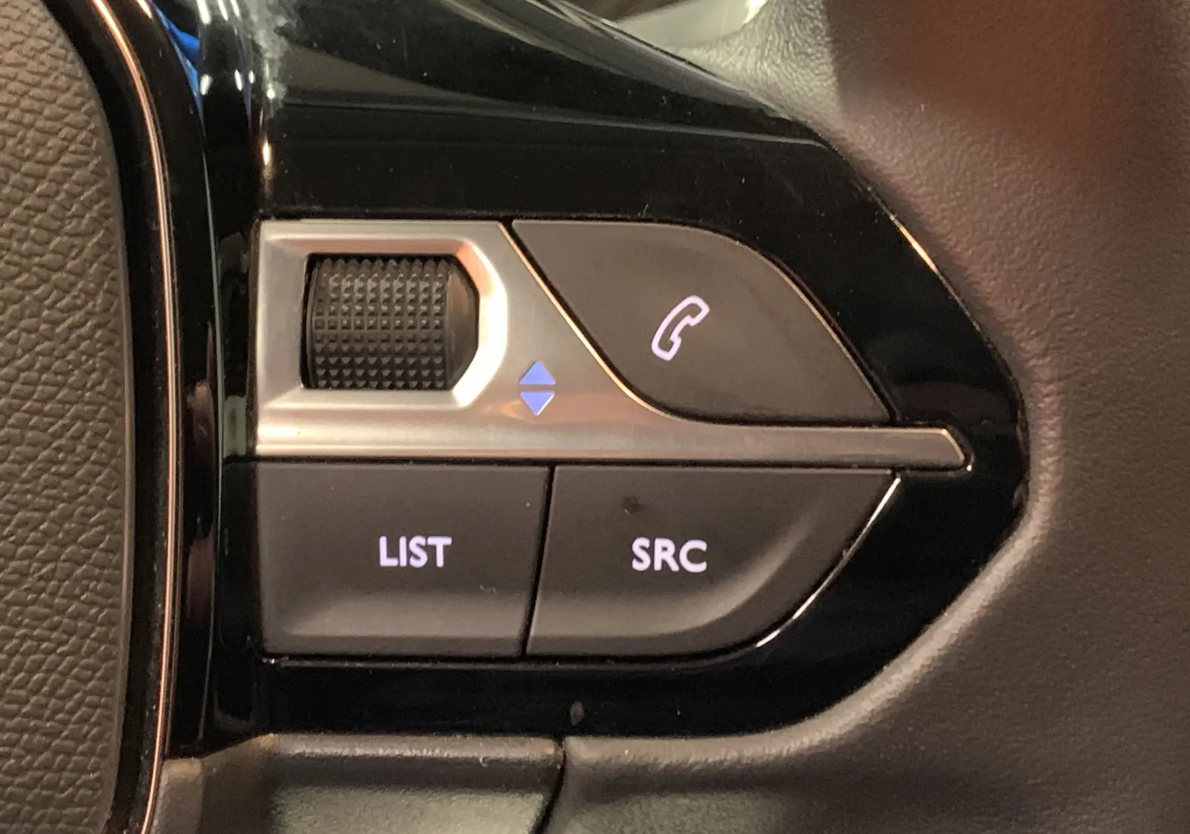 Gros plan sur les commandes au volant côté gauche de la Peugeot 208 gris, avec boutons LIST, SRC et téléphone.