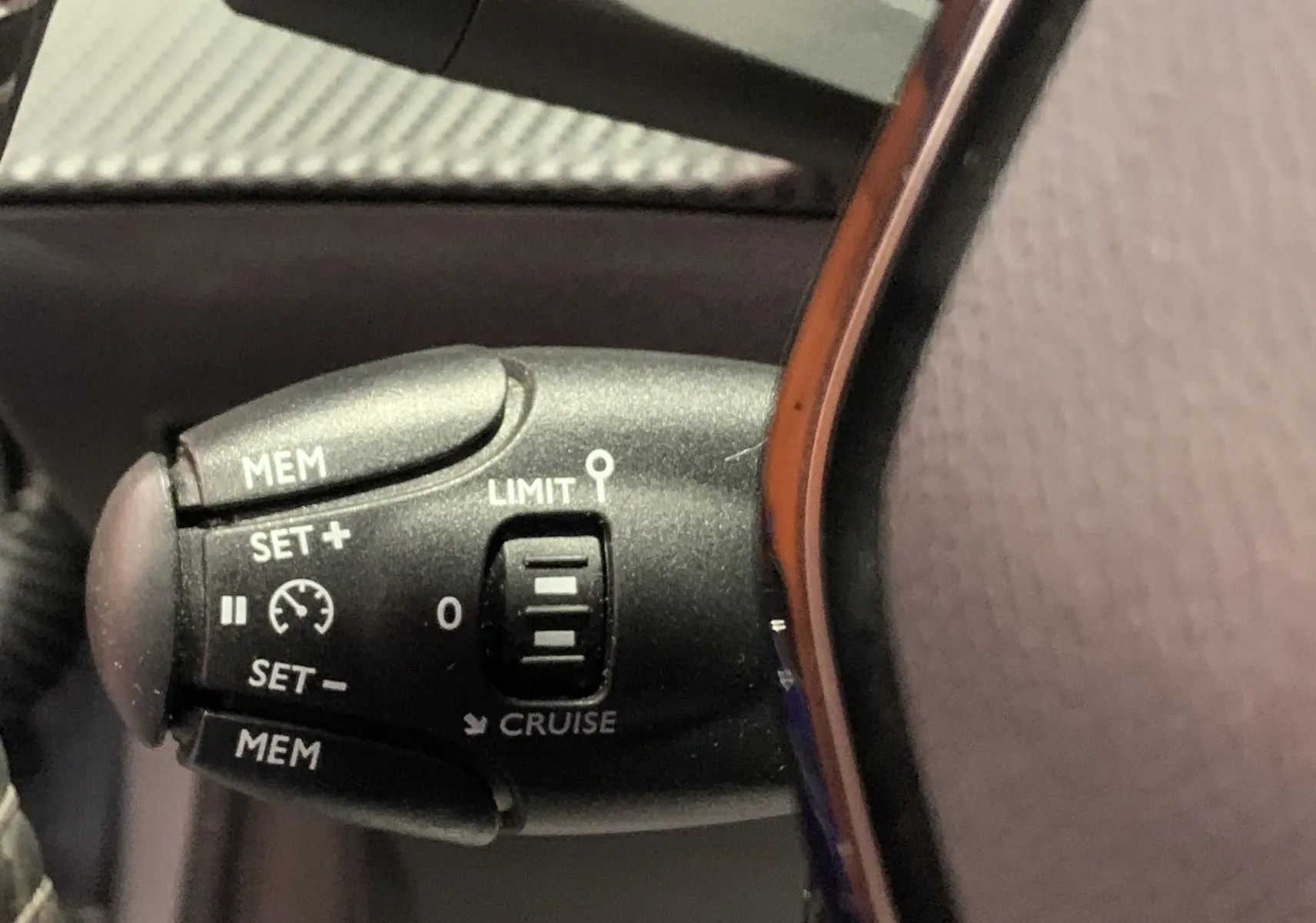 Gros plan sur la commande de régulateur de vitesse à gauche du volant d’une Peugeot 208 gris 2021.