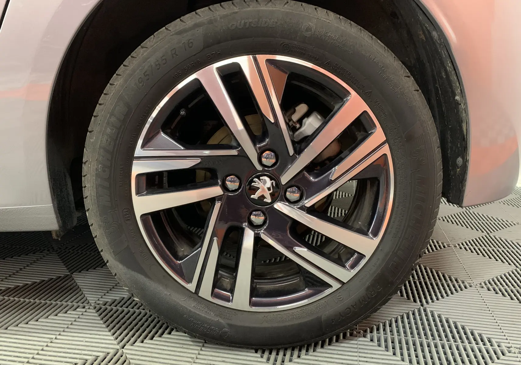 Gros plan sur la roue avant gauche gris métallisé d'une Peugeot 208 PureTech 100 Allure Business avec jante alliage bicolore.