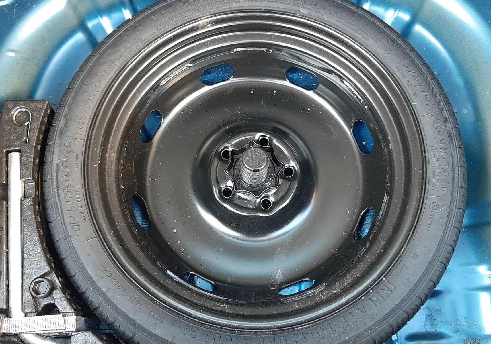 Roue de secours noire dans le coffre bleu d’un Volkswagen T-Roc 1.5 TSI 2022, avec outil de changement visible à gauche.