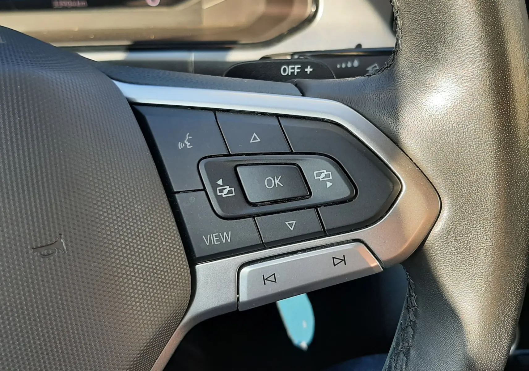 Gros plan sur les commandes multifonctions côté gauche du volant en cuir du Volkswagen T-Roc bleu 2022, avec tableau de bord partiellement visible.