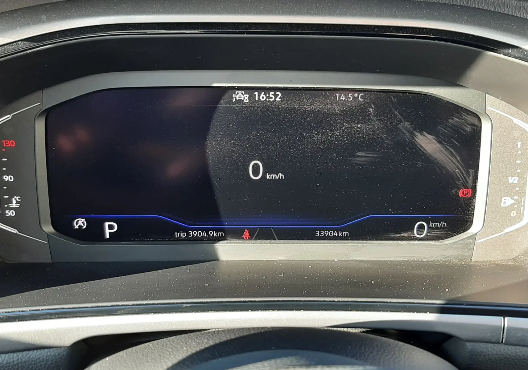 Vue rapprochée du tableau de bord numérique du Volkswagen T-Roc 1.5 TSI bleu, affichant la vitesse à 0 km/h et l'heure.