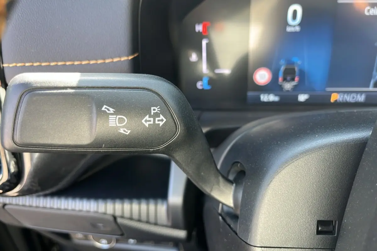 Gros plan sur la manette de clignotants et feux du Ford Ranger PHEV 281 Wildtrak, intérieur noir avec coutures marron.