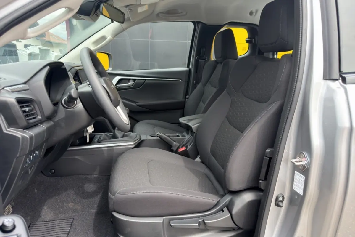 Vue intérieure côté conducteur de l'Isuzu D-MAX 2026 gris Mercury, sièges tissu noirs avec accoudoir central.