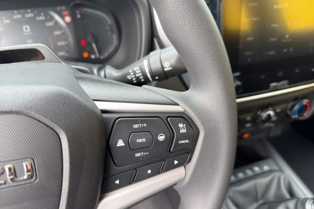 Gros plan sur le volant multifonctions gris du pick-up Isuzu D-MAX 2026 avec commandes de régulateur et tableau de bord flou.