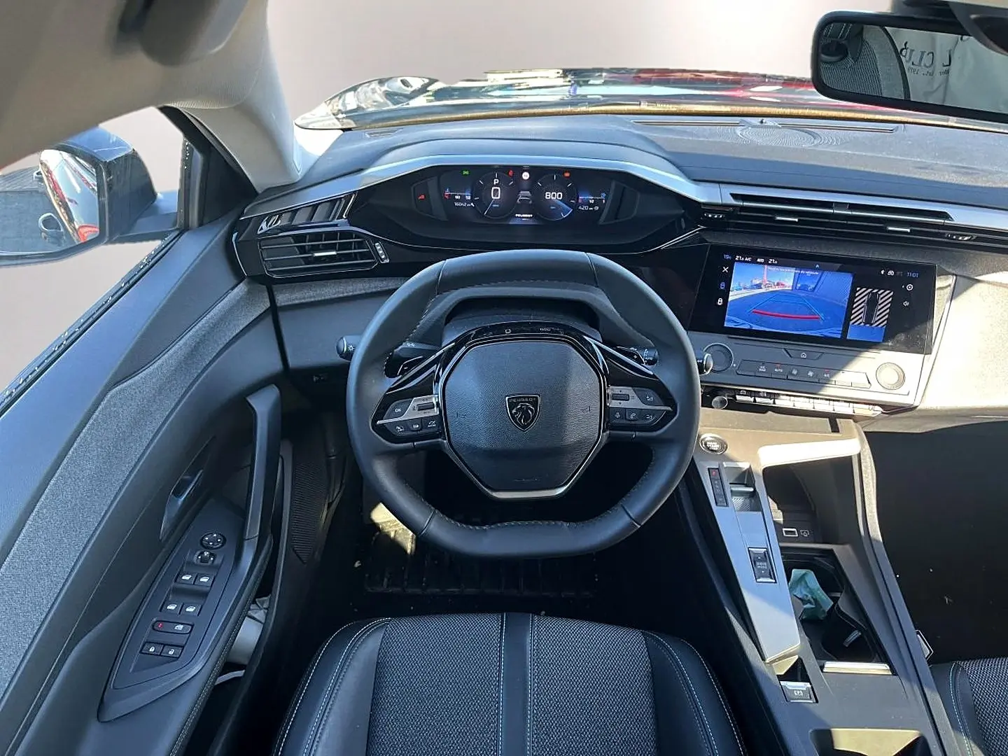 Vue intérieure de face du poste de conduite de la Peugeot 308 noire, avec volant compact et écran tactile affichant la caméra de recul.