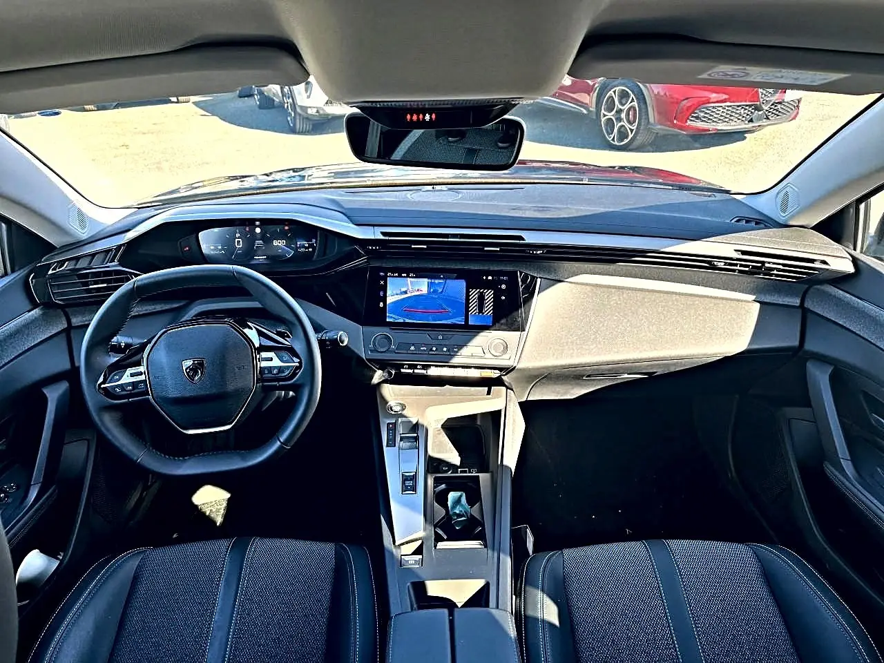 Vue intérieure avant de la Peugeot 308 noire, montrant le tableau de bord digital et l'écran tactile central avec caméra de recul.