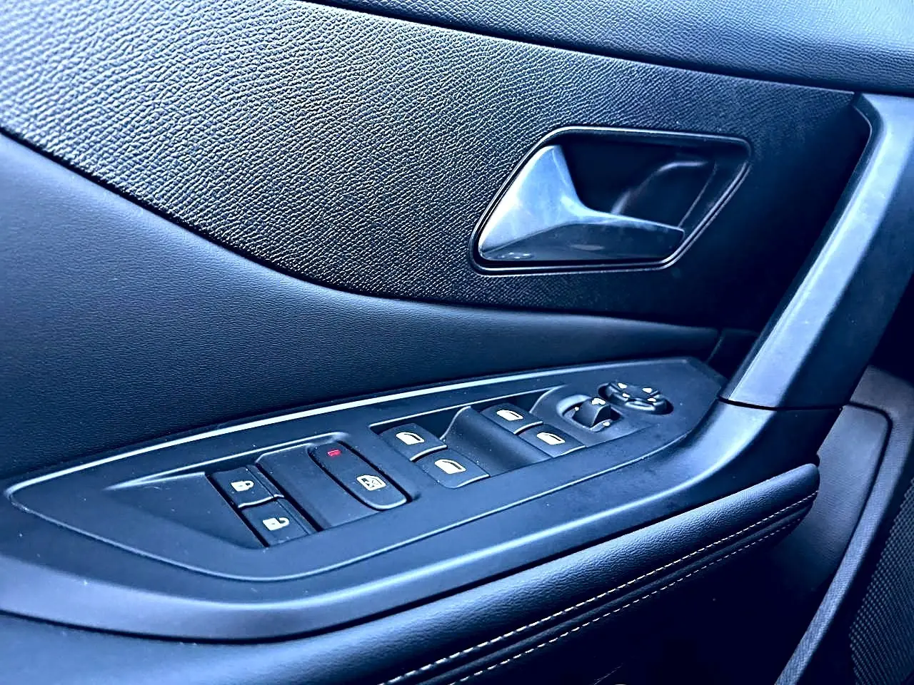 Gros plan sur la commande des vitres et la poignée intérieure côté gauche d’une Peugeot 308 noire, finition 2025.