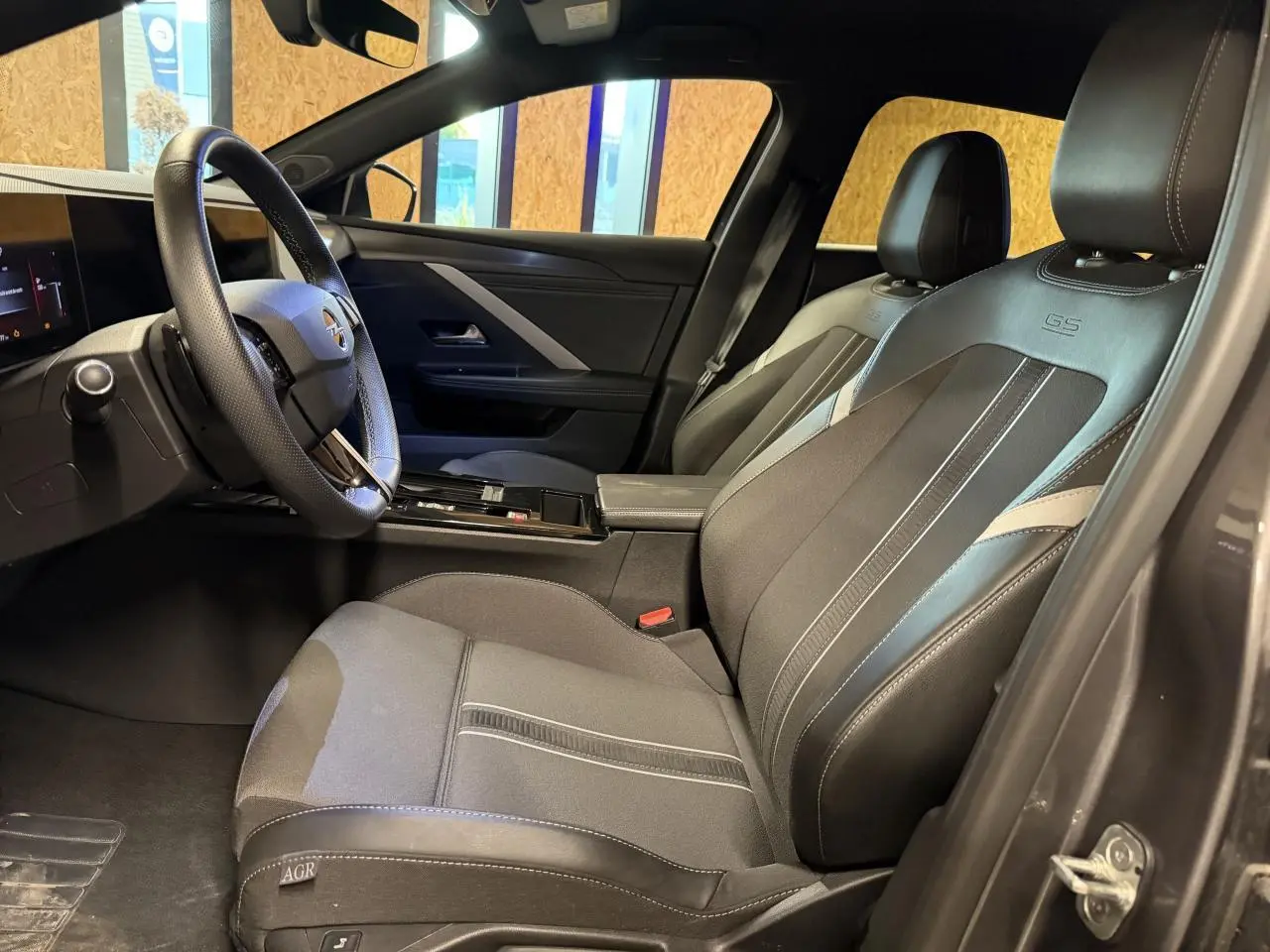 Vue intérieure côté conducteur de l’Opel Astra 2024 avec sièges mixte tissu/TEP noirs et volant cuir perforé.