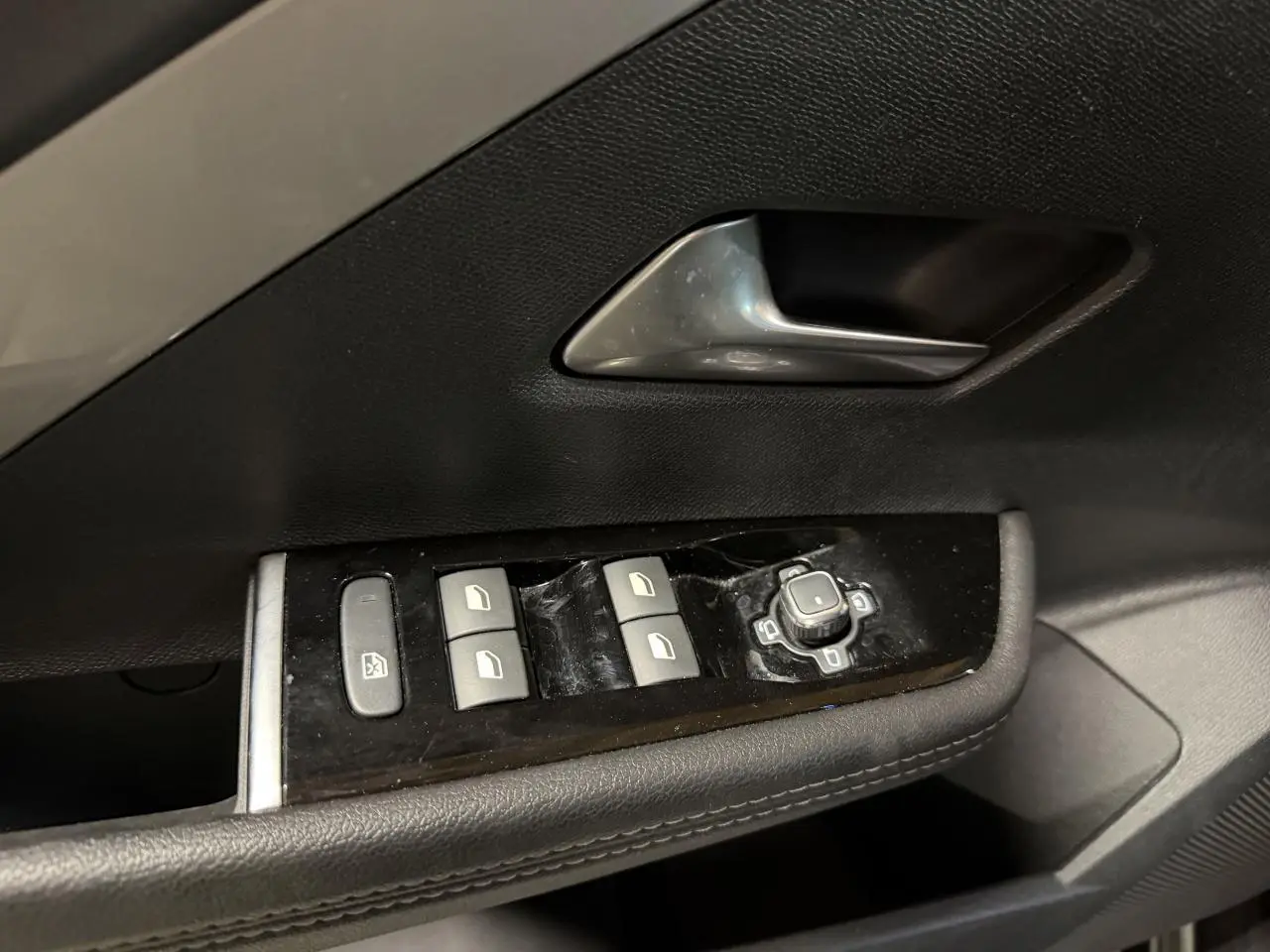 Gros plan sur la commande des vitres et rétroviseurs côté gauche de la porte intérieure noire de l'Opel Astra gris foncé.