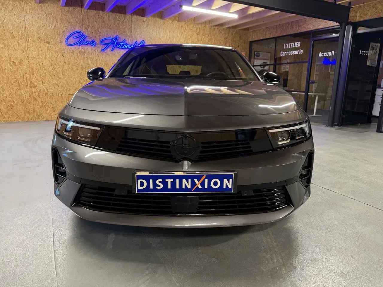 Vue frontale d'une Opel Astra gris foncé avec calandre noire et pare-chocs avant sportif dans un garage.