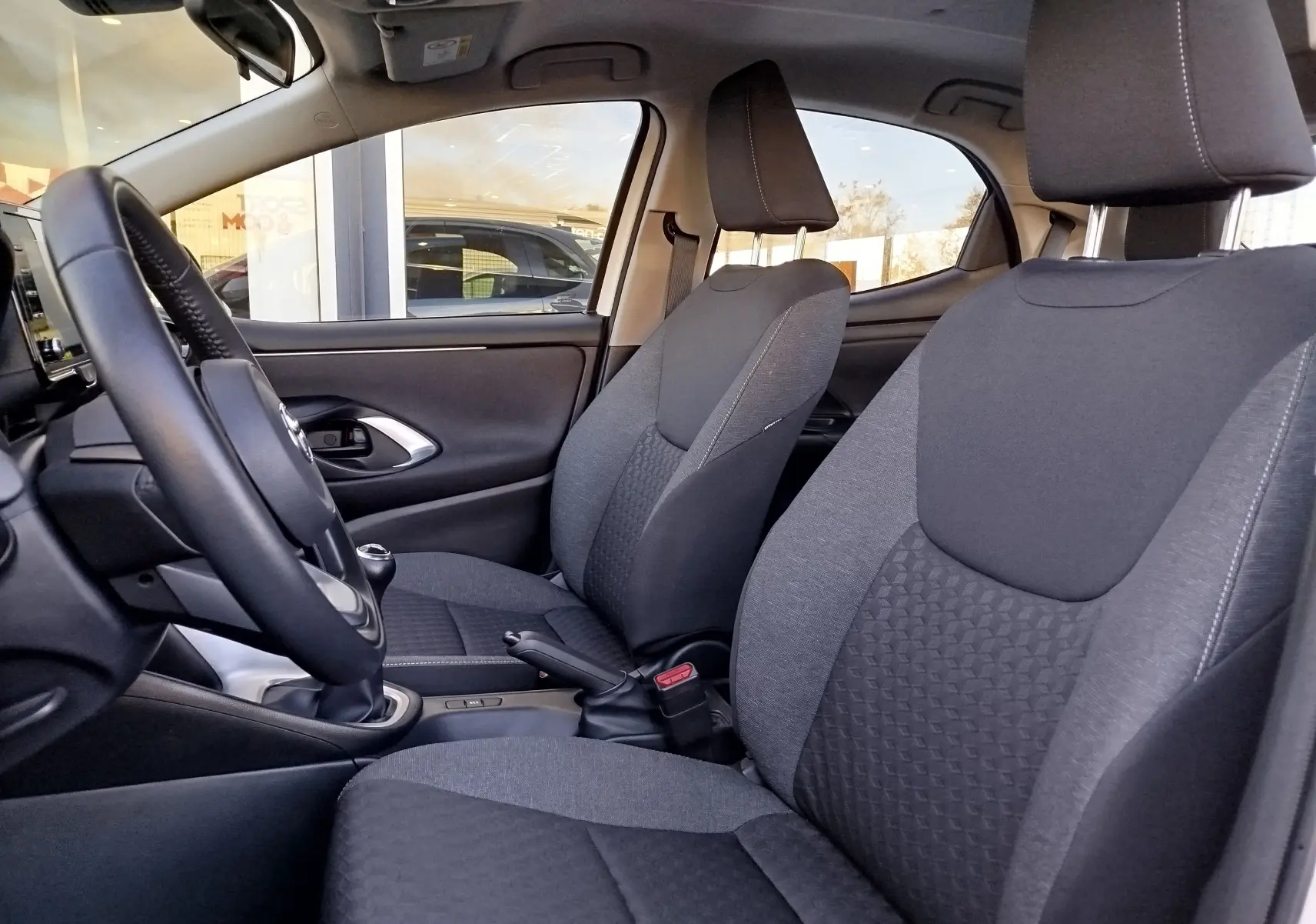 Vue intérieure côté gauche de la Toyota Yaris 2023, sièges tissu gris et volant avec boîte manuelle visible.
